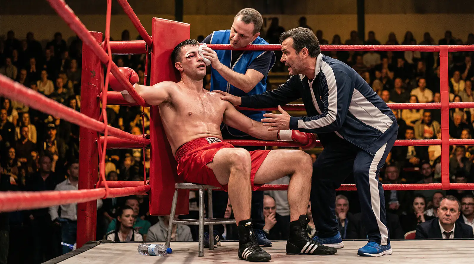 Boxer in der Ringecke während einer Rundenpause mit Trainer und Publikum im Hintergrund